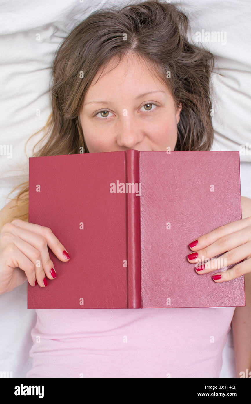 Assonnato ragazza posa in un letto con un libro nelle sue mani Foto Stock