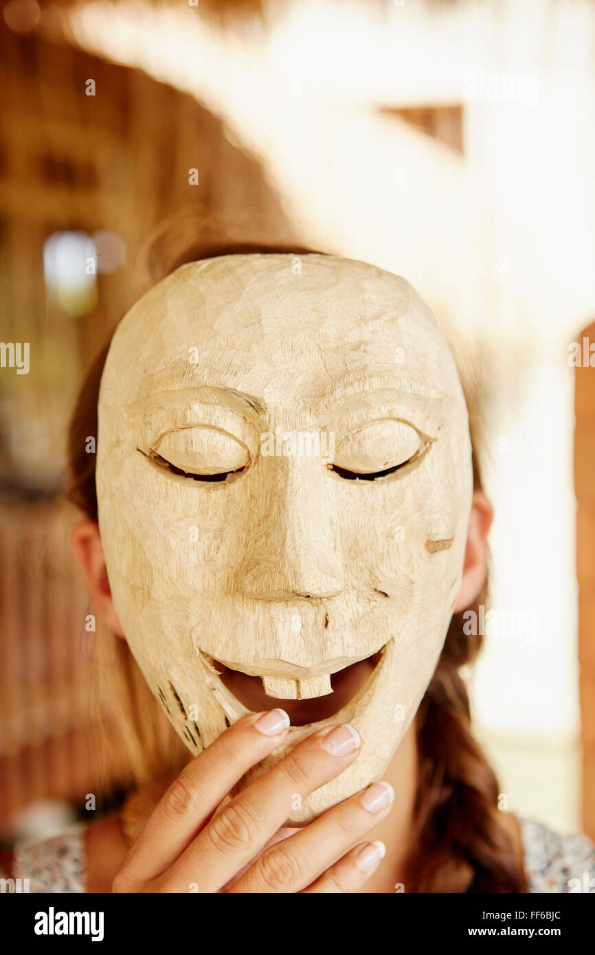 Una persona con in mano una maschera di legno sulla parte anteriore del suo viso. Foto Stock