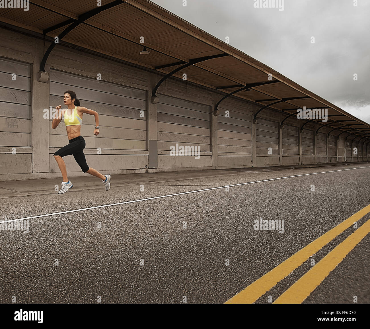 Una donna che corre lungo una strada urbana, bracci di lavoro e gambe di estensione. Foto Stock