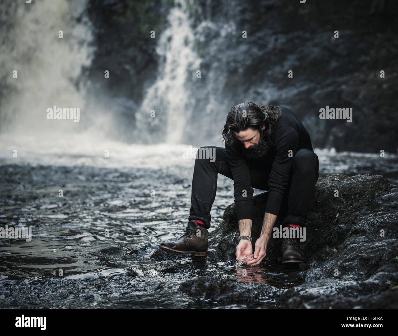 Un uomo di lavarsi le mani in un ruscello di montagna. Foto Stock