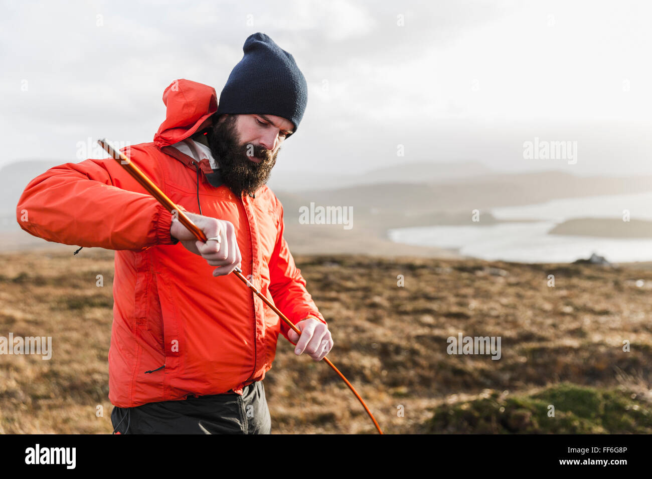 Un uomo in un paesaggio aperto, tenendo un palo della tenda. Foto Stock