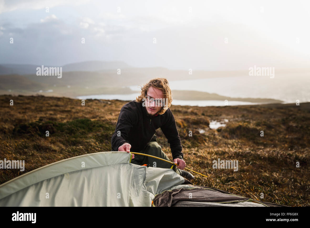 Un uomo di alimentazione di un palo della tenda nella tenda di tessuto in uno spazio aperto. Foto Stock