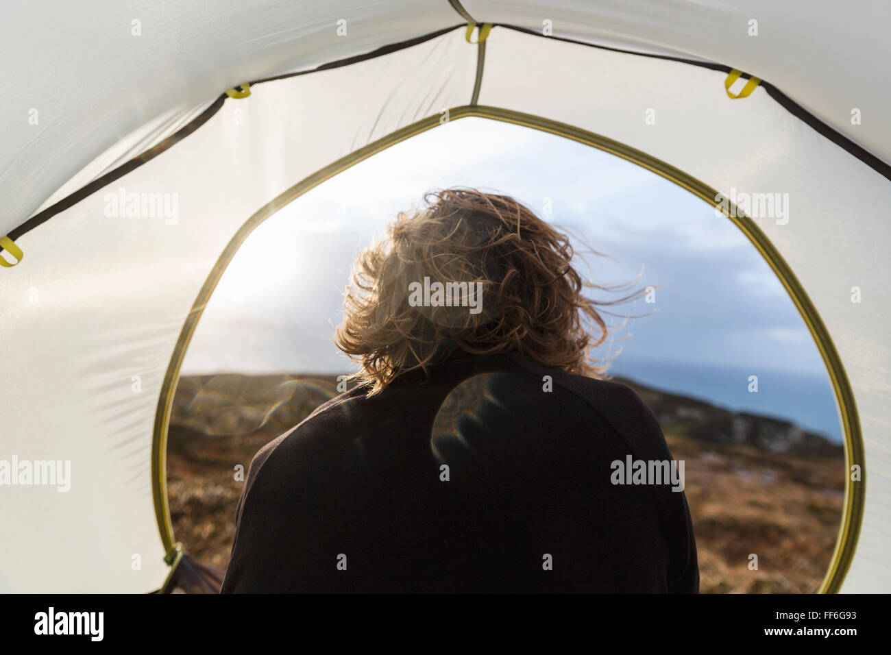 Un uomo seduto al riparo di una tenda guardando fuori. Foto Stock