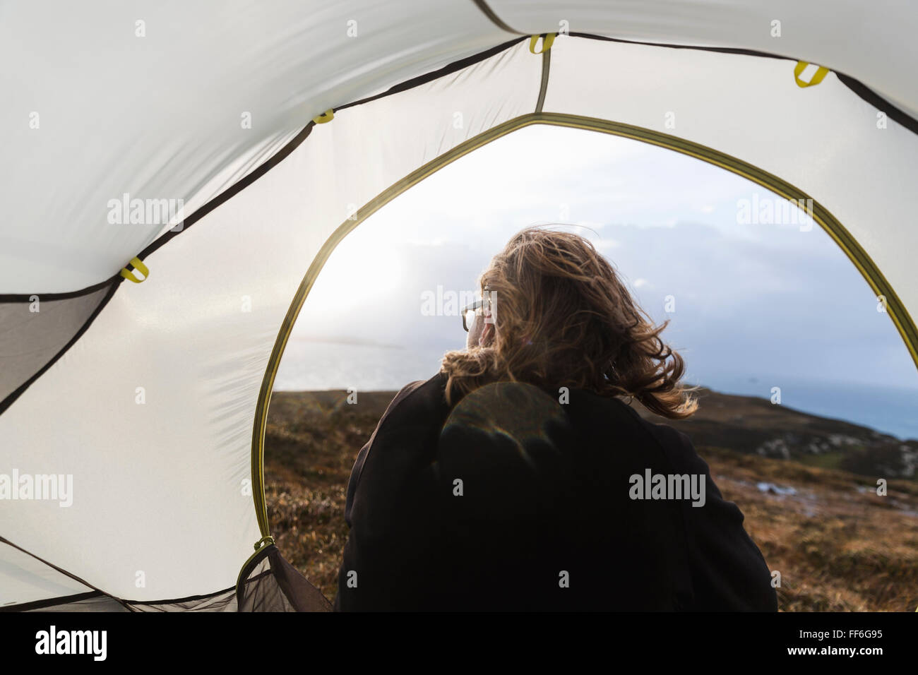 Un uomo seduto al riparo di una tenda guardando fuori. Foto Stock