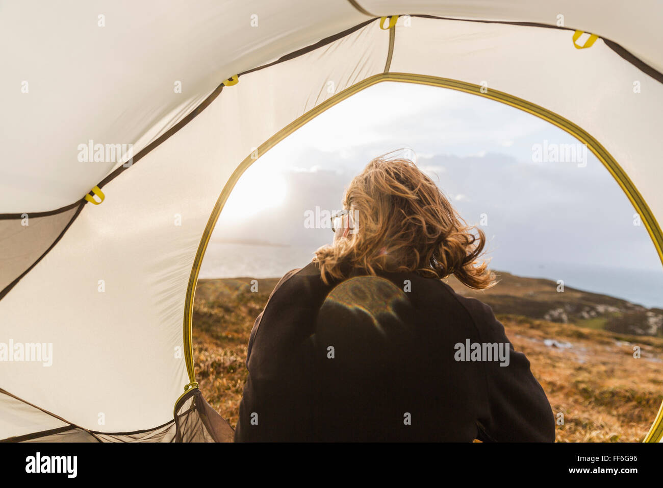Un uomo seduto al riparo di una tenda guardando fuori. Foto Stock
