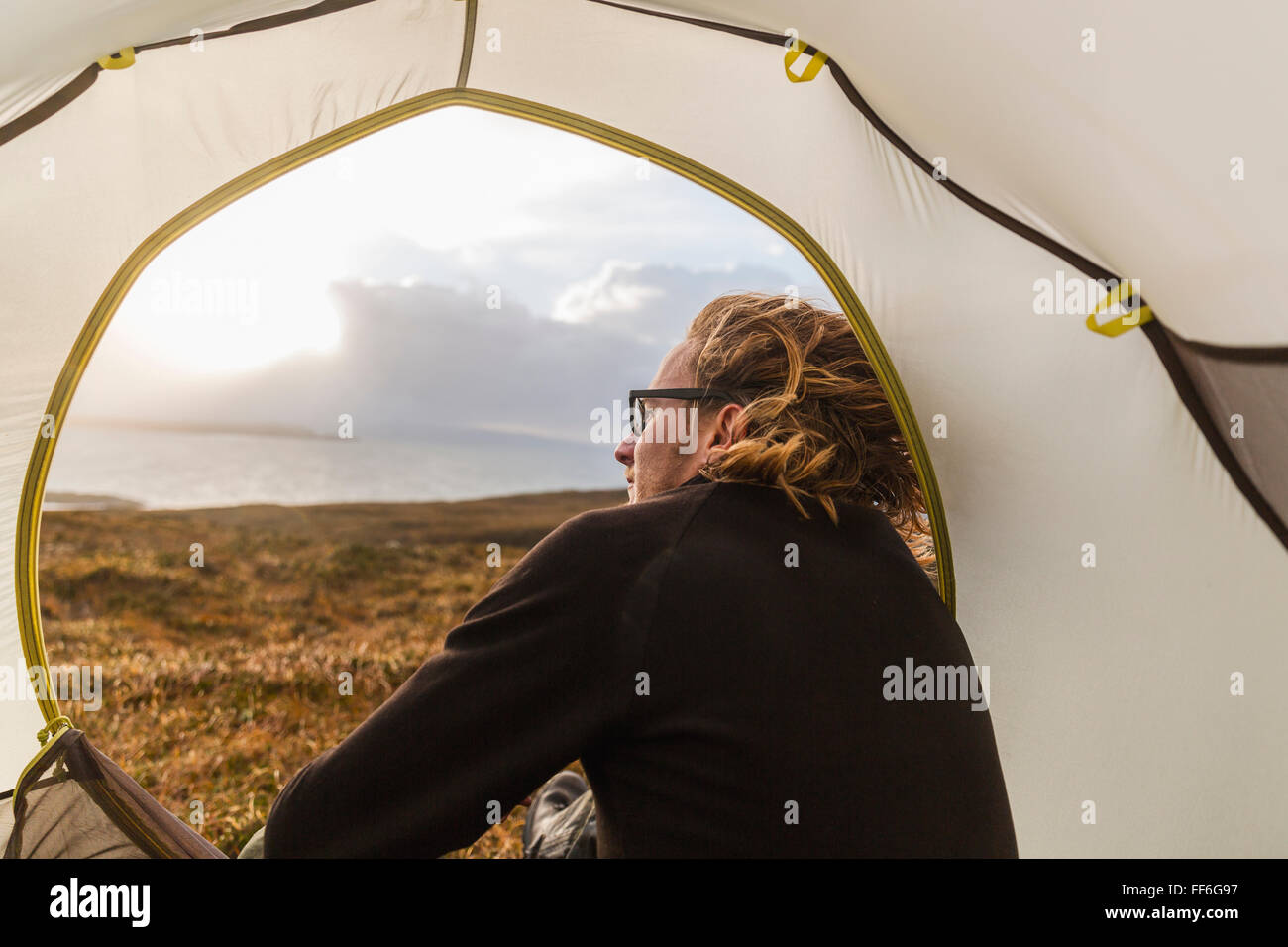 Un uomo seduto al riparo di una tenda guardando fuori. Foto Stock