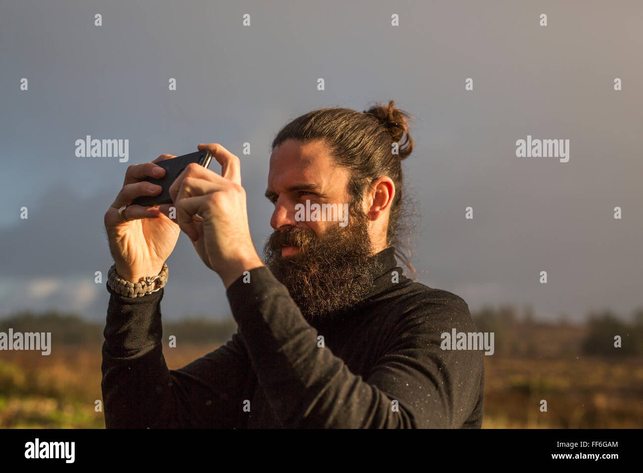 Un uomo che sta usando un telefono intelligente per scattare una fotografia sotto un cielo grigio. Foto Stock
