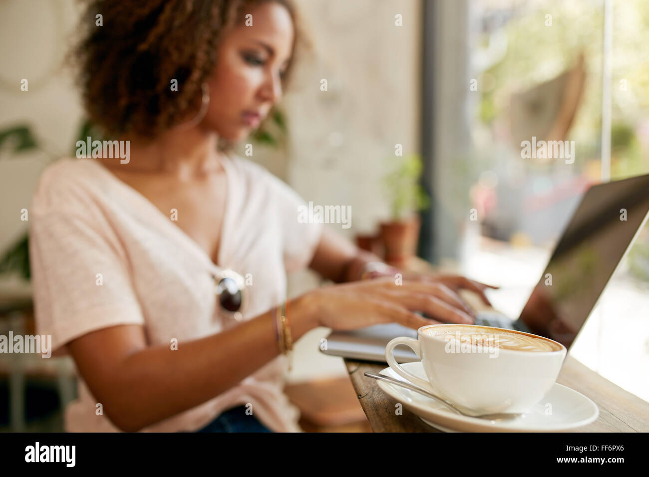 Tazza di cappuccino fresco sul tavolo con una giovane donna che lavorano su computer portatile in background. La messa a fuoco della tazza di caffè presso il cafe. Foto Stock