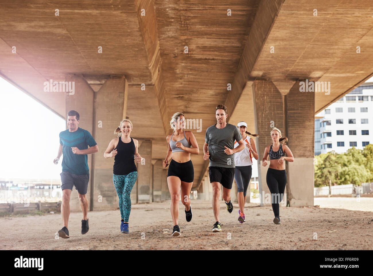 Gruppo di atleti in esecuzione su una strada sotto il ponte nella città. Giovani uomini e donne jogging, formazione insieme nella mattina. Foto Stock