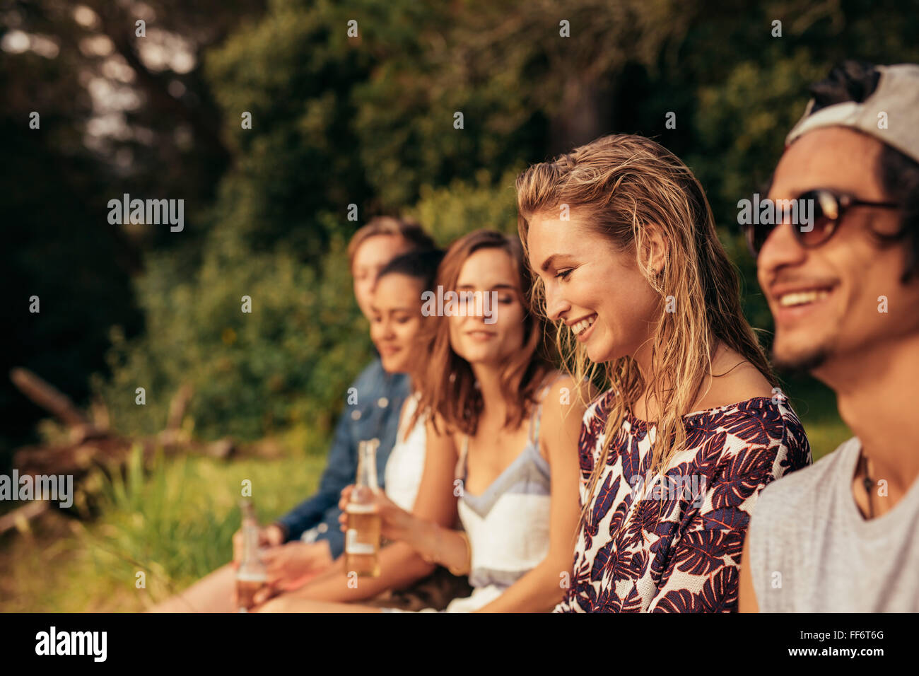 Ritratto di felice giovane donna seduta con i suoi amici da un lago. Giovani appendere fuori a lago. Foto Stock