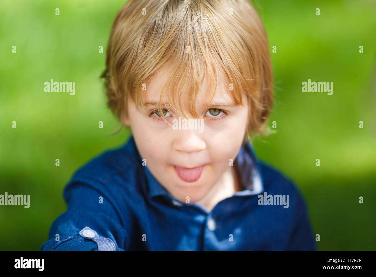 Ritratto di un piccolo ragazzo carino che mostra la linguetta sullo sfondo verde Foto Stock