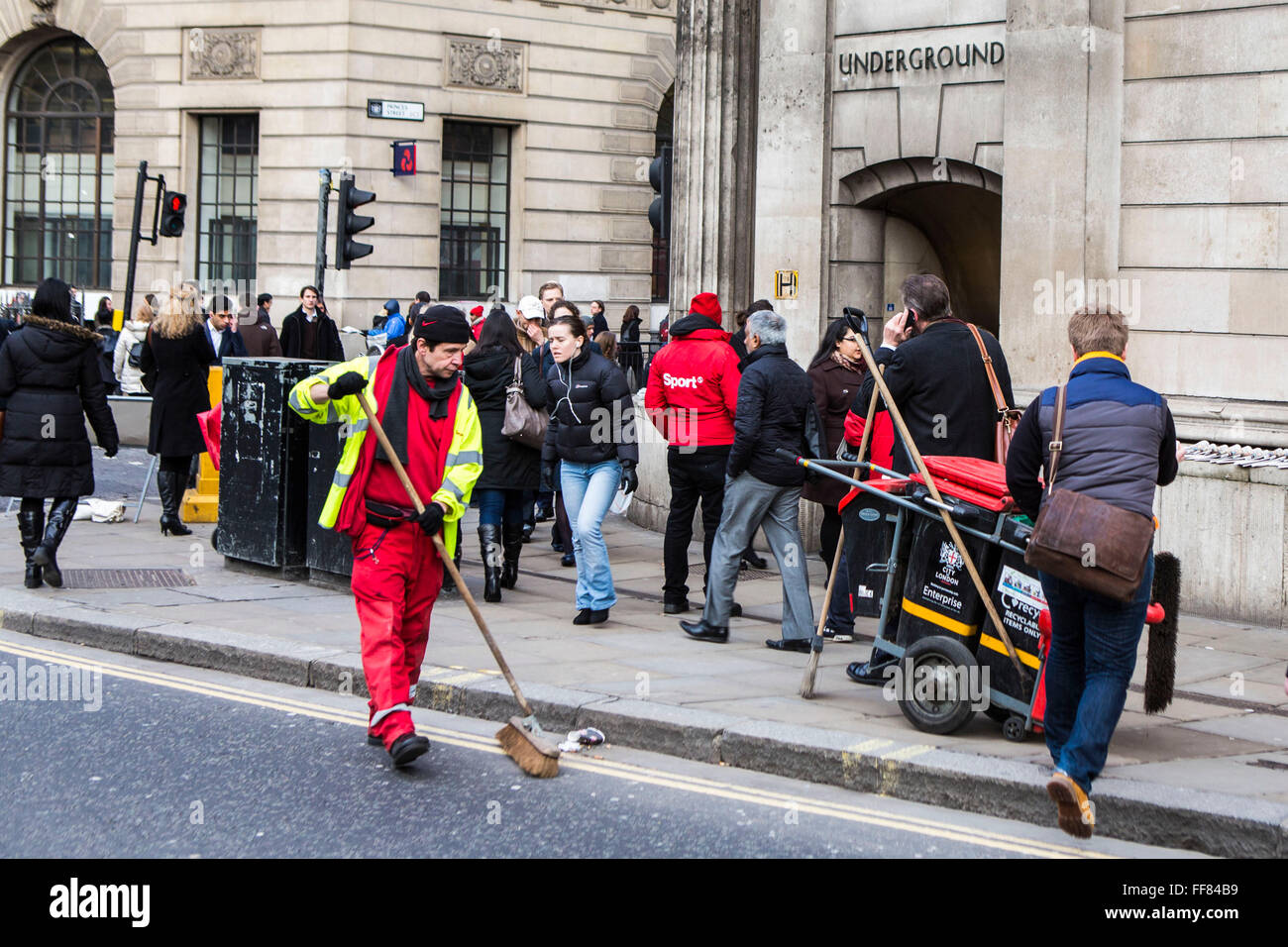 Un British street cleaner spazza la strada per pulire e rifiuti raccolti tra i molti pendolari presso la banca occupato incrocio nel centro di Londra, Regno Unito. La strada di servizio di pulizia è fornito da la City of London Corporation che è municipale il corpo direttivo. Foto Stock