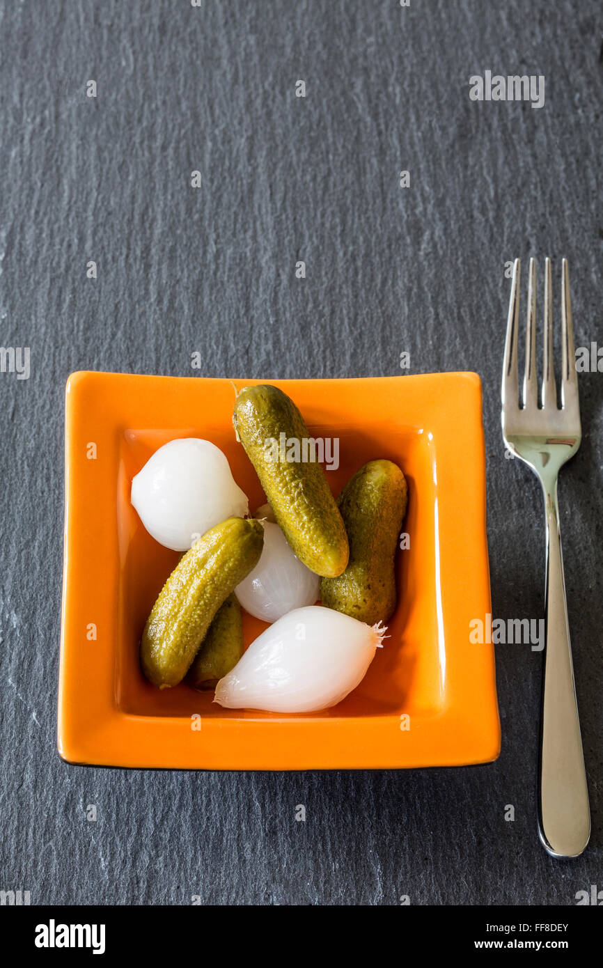 Pellicola argentea cipolle e cetriolini in una piccola ciotola di vetro al buio su un sfondo di ardesia Foto Stock