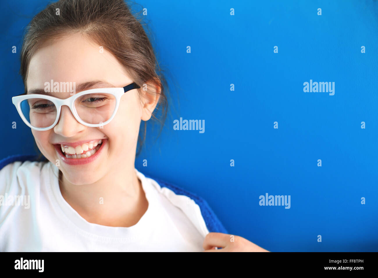 Bella ragazza sorridente in vetri bianchi su sfondo blu. Sorriso sincero, bambino felice. Sorriso, splendido sorriso bianco Foto Stock