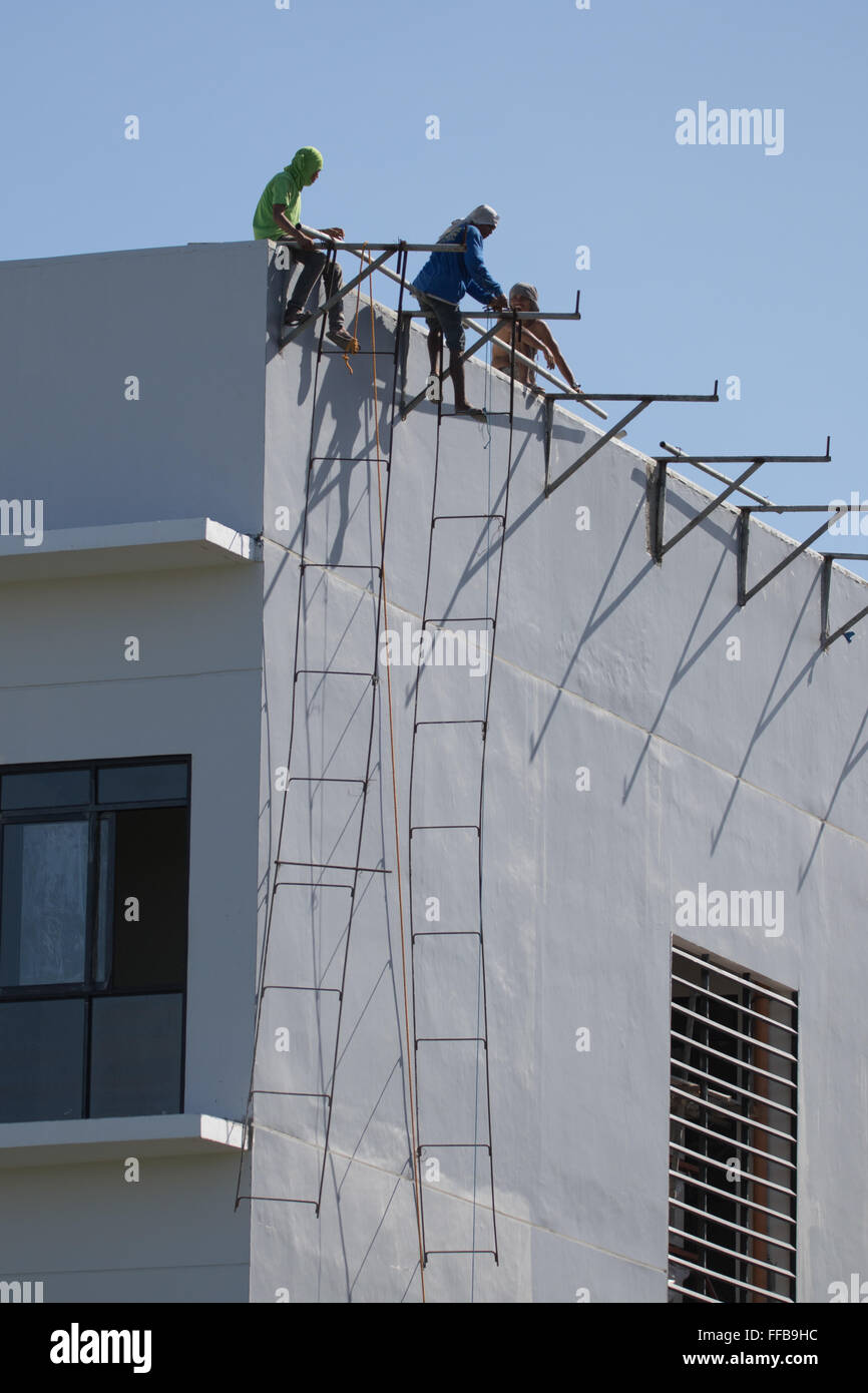 Una scena comune nelle Filippine edilizia - costruzione di lavoratori appendere precariamente dal ferro da stiro realizzato localmente e saldare le scale. Foto Stock
