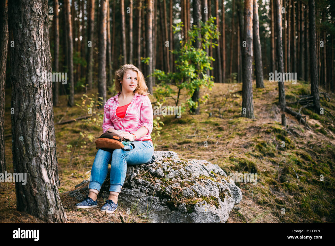 Bella la dimensione più giovane donna in camicia seduta su pietra inSummer Forest Foto Stock