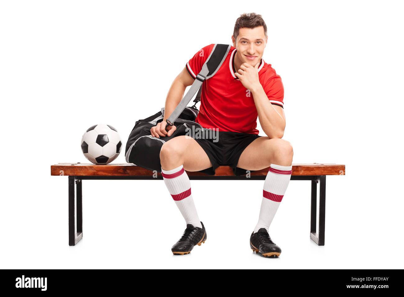 Giovane calciatore seduto su una panca in legno e guardando la telecamera isolata su sfondo bianco Foto Stock Giovane calciatore seduto su una panca in legno e guardando la telecamera isolata su sfondo bianco Foto Stock