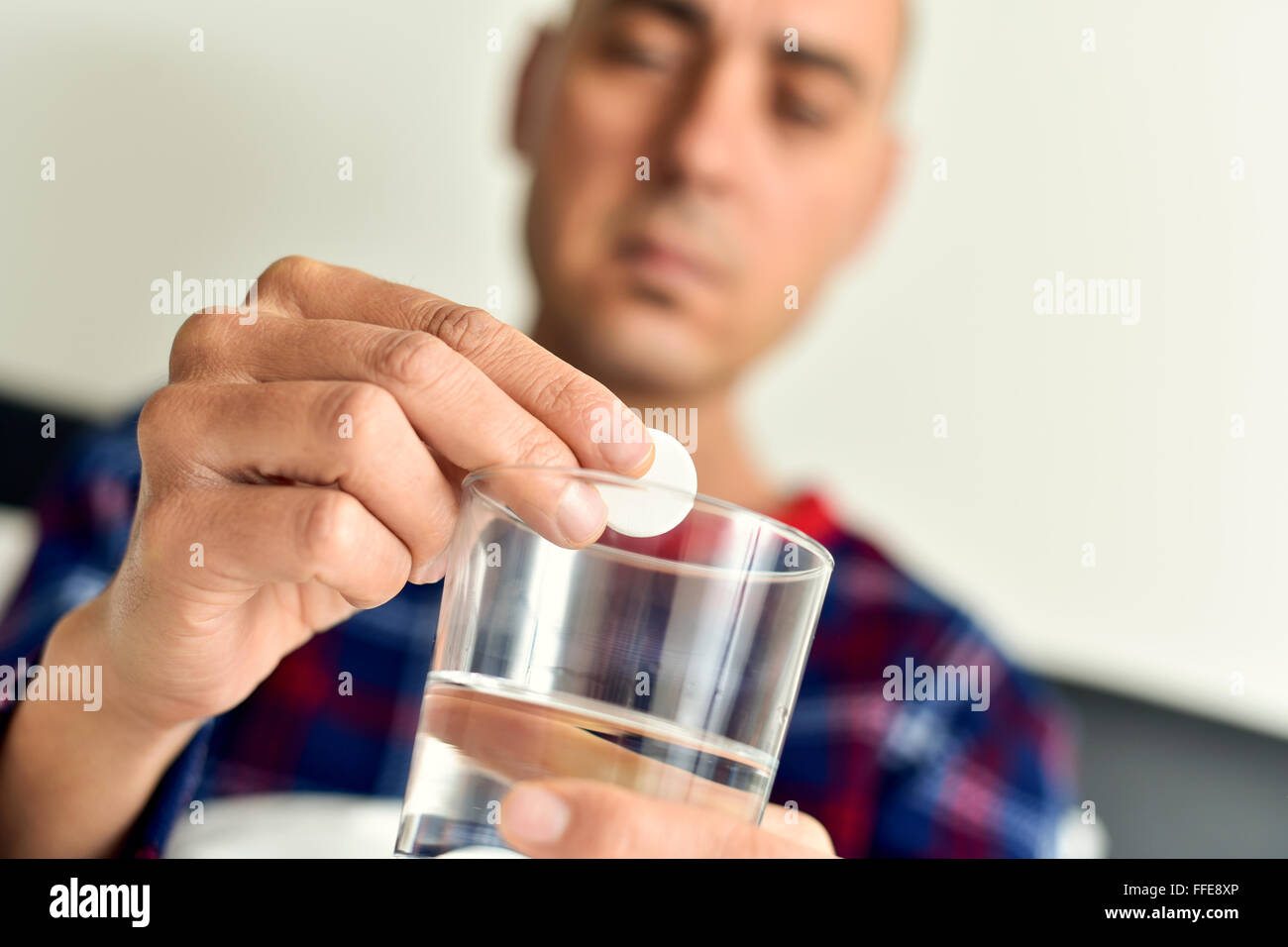 Primo piano di un giovane uomo caucasico in pigiama nel letto circa a mettere una compressa effervescente in un bicchiere con acqua Foto Stock