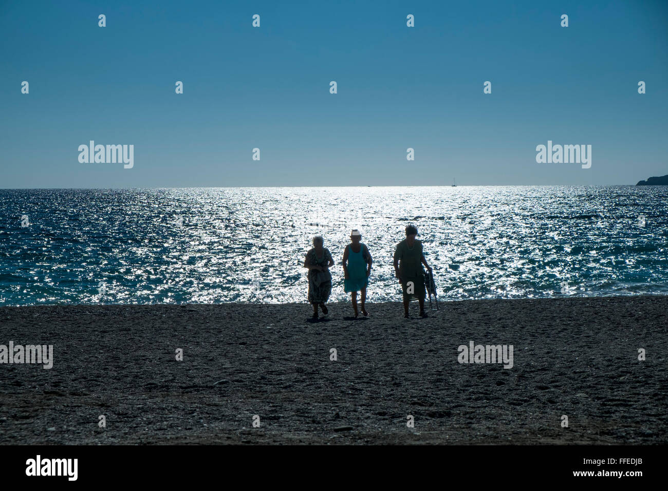 Tre donne che camminano sulla spiaggia nel tardo pomeriggio, retroilluminate da un mare scintillante e soleggiato. Almuñécar, Provincia di Granada, Andalusia. Spagna Foto Stock