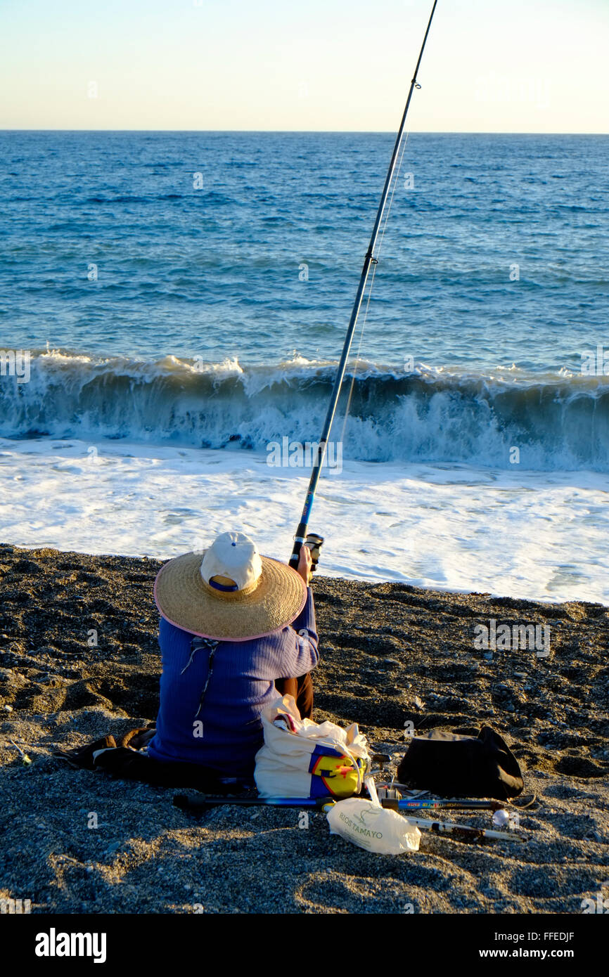 Lone angler seduto e la pesca dalla spiaggia come il sole scende. Almuñécar, Granada, Andalusia. Spagna Foto Stock