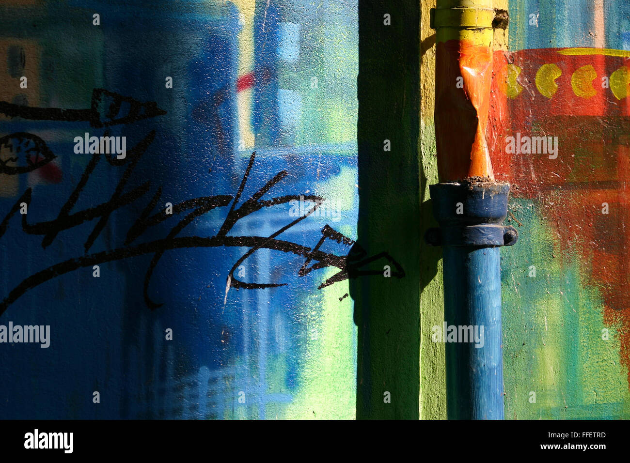 Coloratissimo graffito su una parete con una vecchia tubazione di pioggia con forte contrasto di sera sun Foto Stock