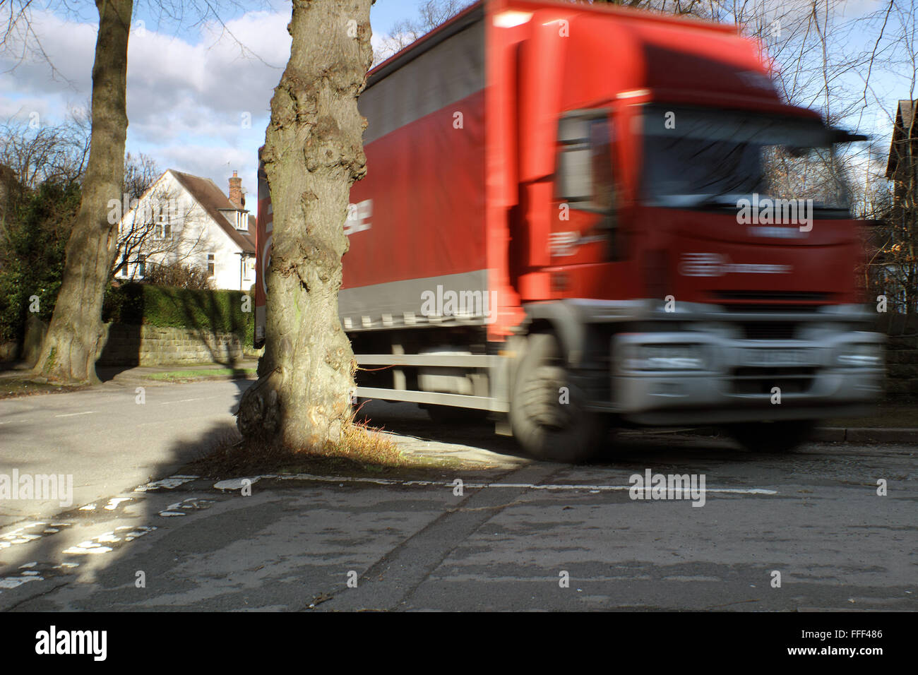 Un camion rigidi mediante un albero che cresce nel mezzo di un incrocio stradale su una strada alberata in un verde sobborgo di Sheffield, Yorkshire Regno Unito Foto Stock