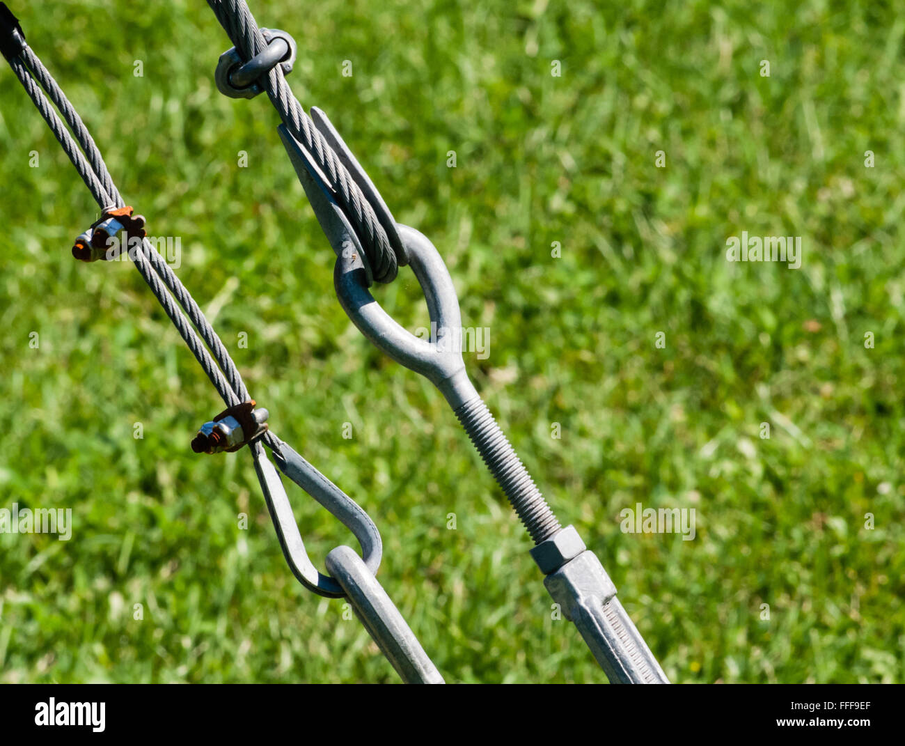 Due ristrette di cavi metallici e anelli di tenuta di ciascun altro e fissato con le staffe e gli equipaggi, contro erba verde dello sfondo. Foto Stock