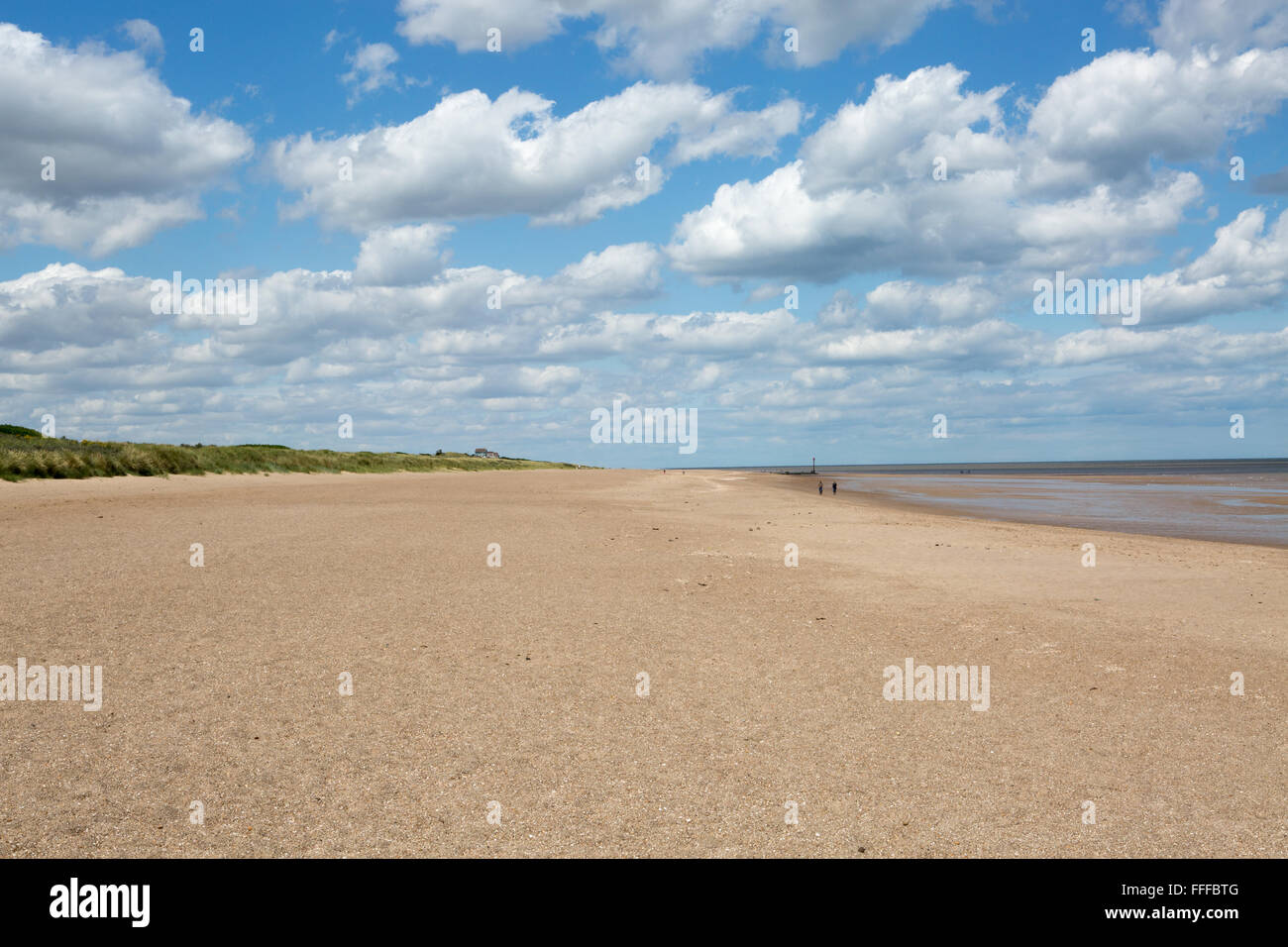 Due persone che passeggiano lungo una spiaggia di sabbia in una soleggiata giornata estiva con la bassa marea, Mablethorpe Beach, Lincolnshire, England, Regno Unito Foto Stock
