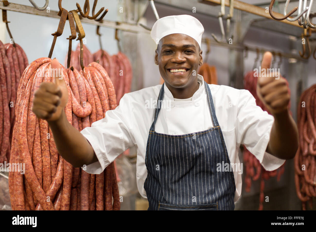 Allegro giovane americano africano butcher pollice in su in camera fredda Foto Stock