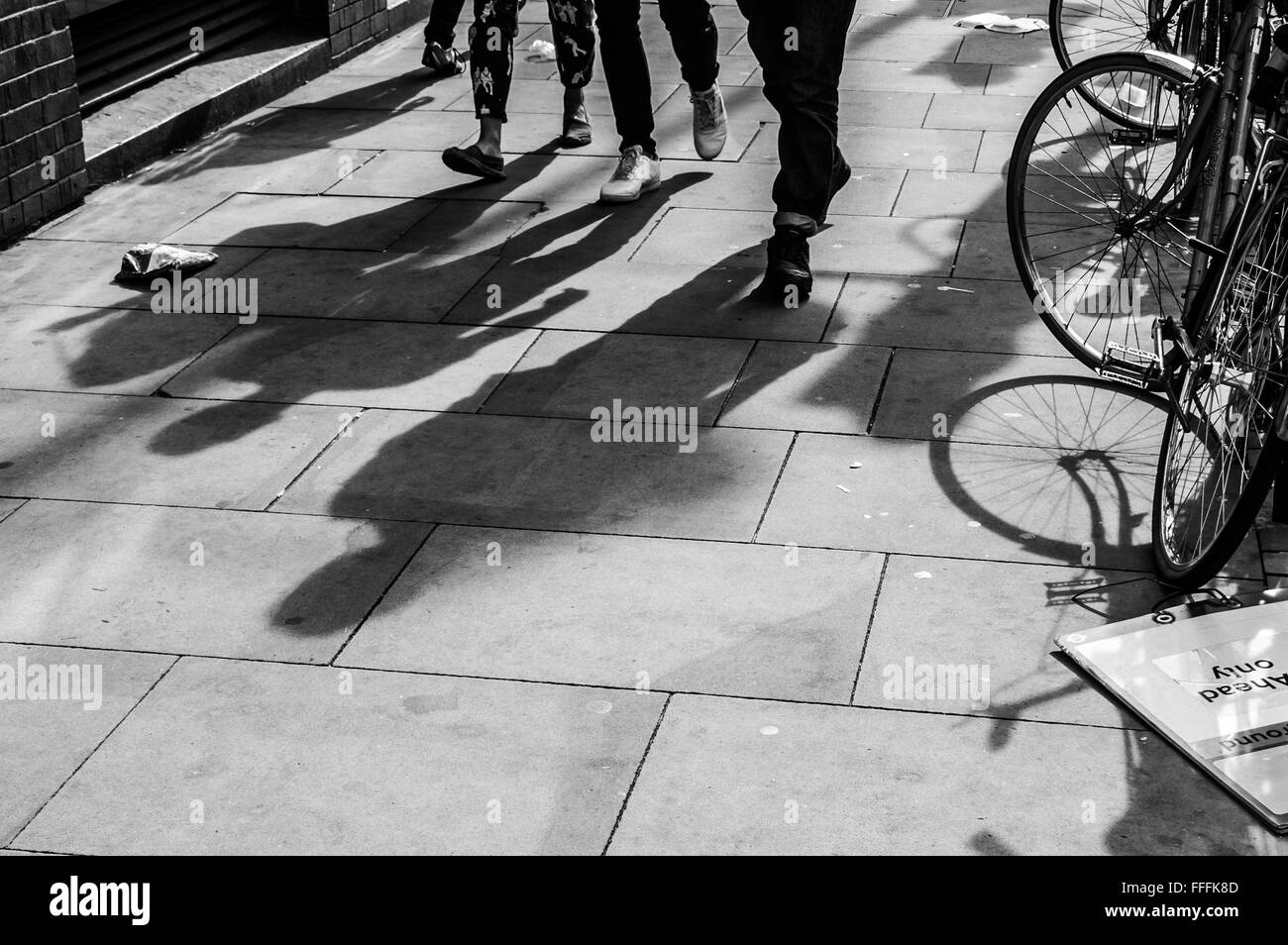 Ombre di tre piedi pedoni proiettata sul marciapiede con la bicicletta sul lato Foto Stock