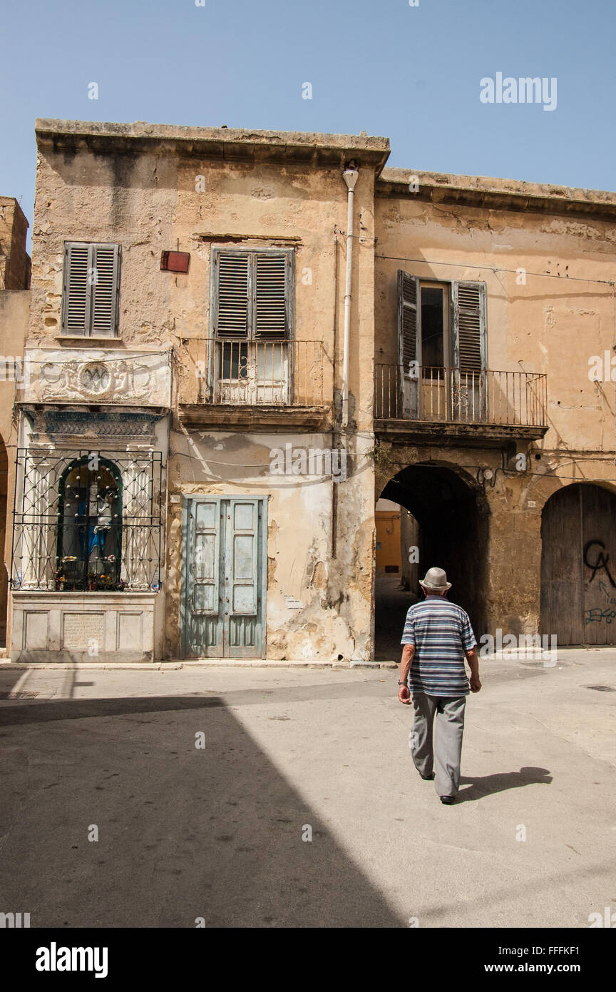 Vecchio italiano uomo a camminare tra fatiscenti case nel quartiere medievale di marsala, Sicilia, Italia. Foto Stock