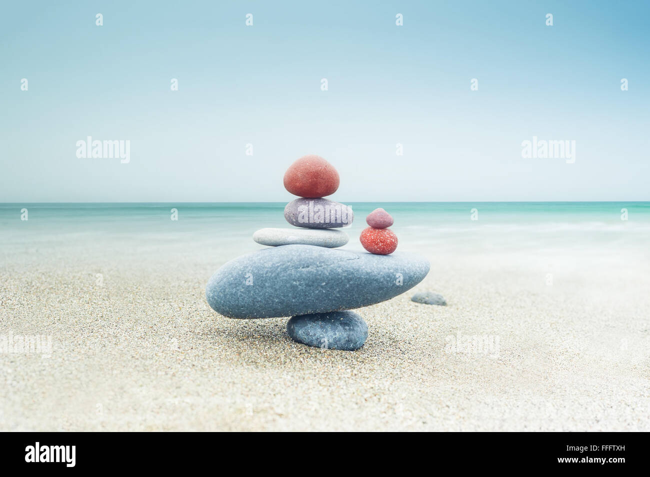 Bilanciamento zen colorati piramide di pietre sulla spiaggia di sabbia sotto il cielo blu. La bellissima natura e concetto spirituale Foto Stock