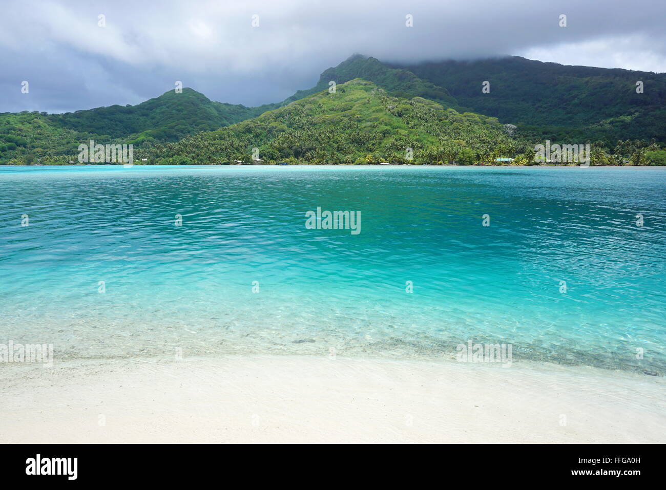 Paesaggio di Huahine isola vista da una spiaggia di sabbia bianca con acqua turchese in primo piano, oceano pacifico, Polinesia Francese Foto Stock