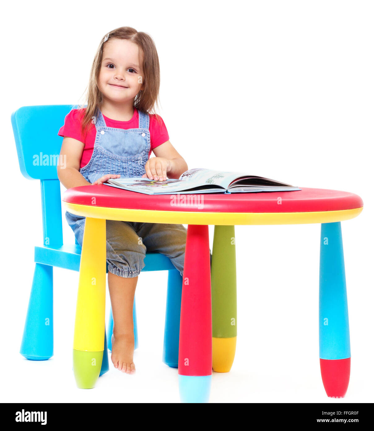 Tre anni ragazza bambino seduto a tavola e la lettura di un libro, isolato su bianco Foto Stock