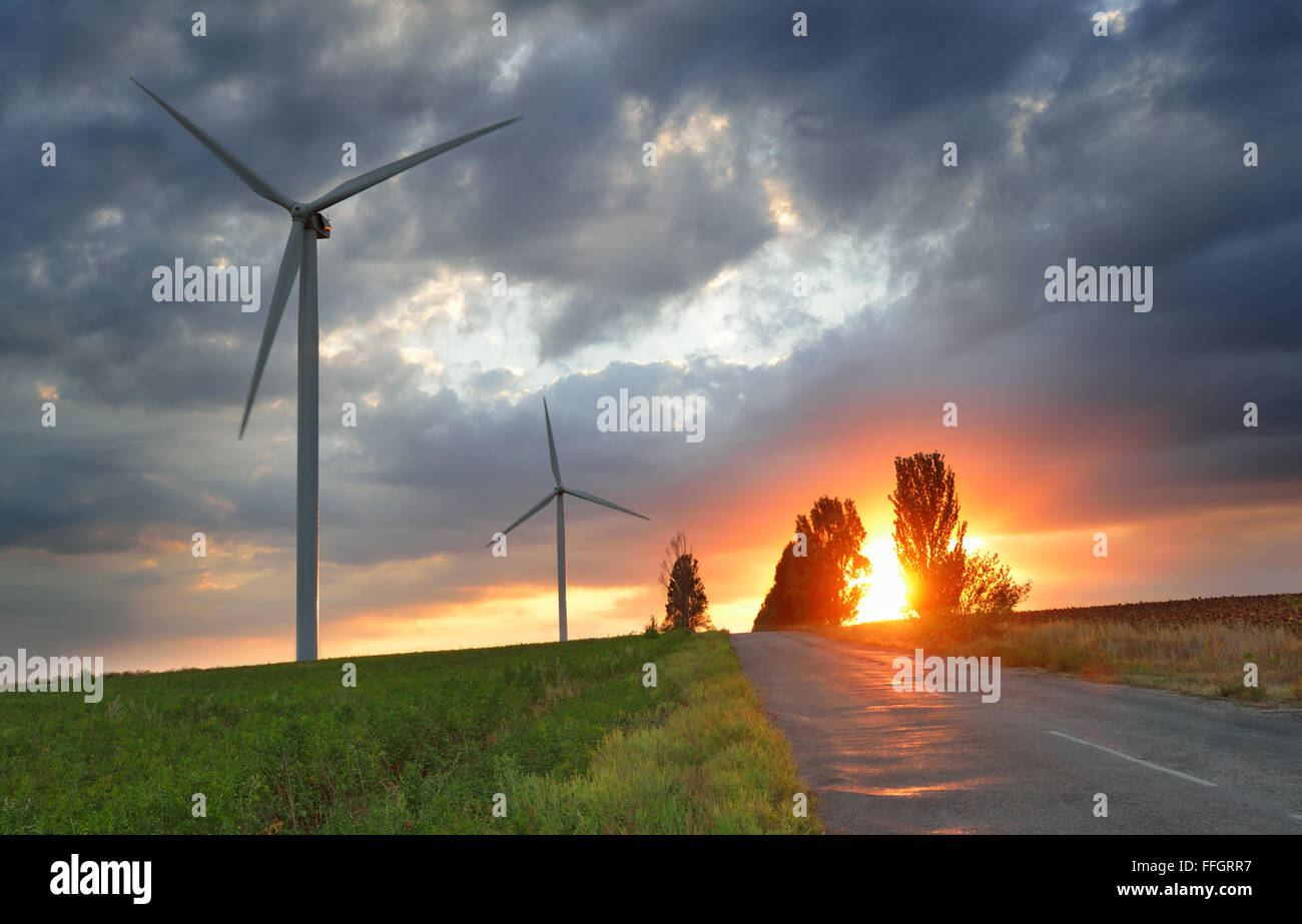 Vecchia strada e delle turbine a vento contro il drammatico il cielo al tramonto Foto Stock