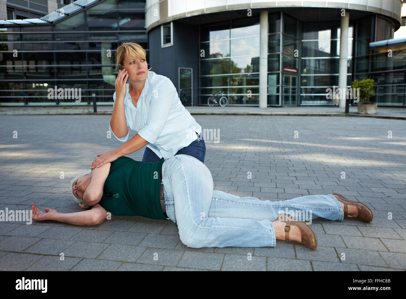 Passerby vicino inconscio senior donna fare chiamate di emergenza Foto Stock