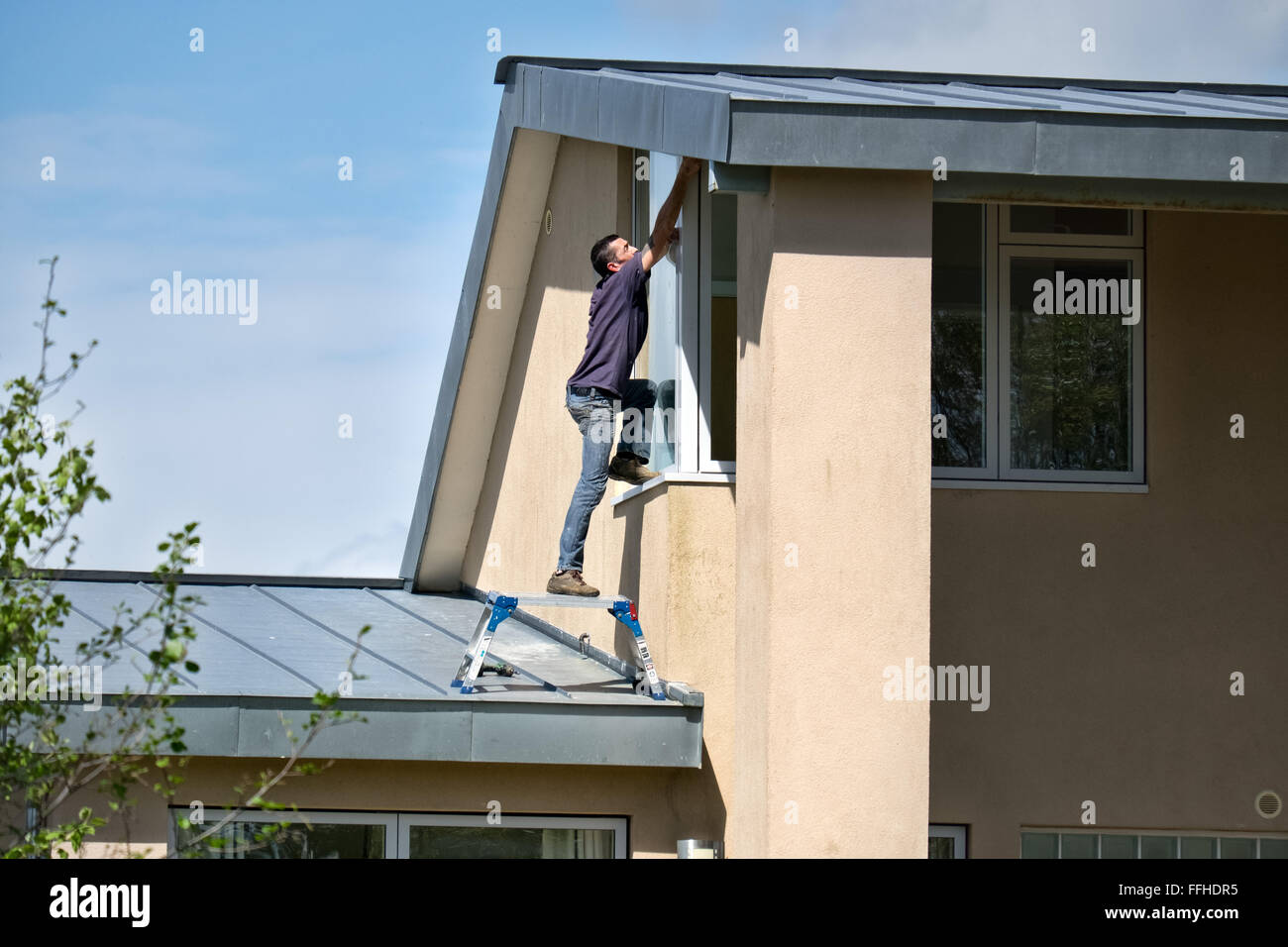 Un sconsiderato proprietario di casa a rischiare la vita & arto su un tetto alto, cercando di mantenere la sua proprietà Foto Stock