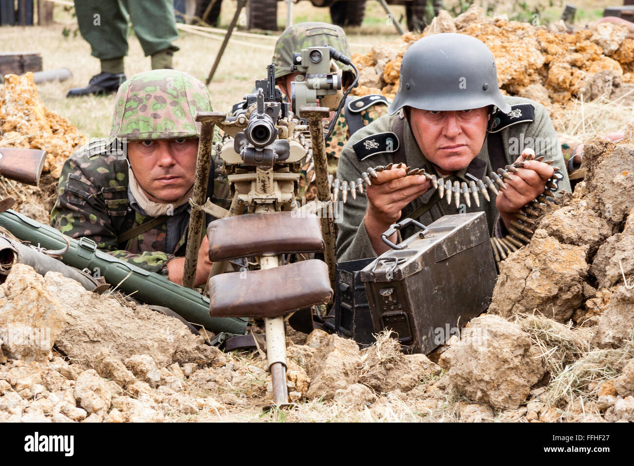 La seconda guerra mondiale la rievocazione. Due Waffen SS di uomini in uniforme di mimetizzazione, dietro la mitragliatrice con canna puntando al visualizzatore, contatto visivo. Close-up. Foto Stock