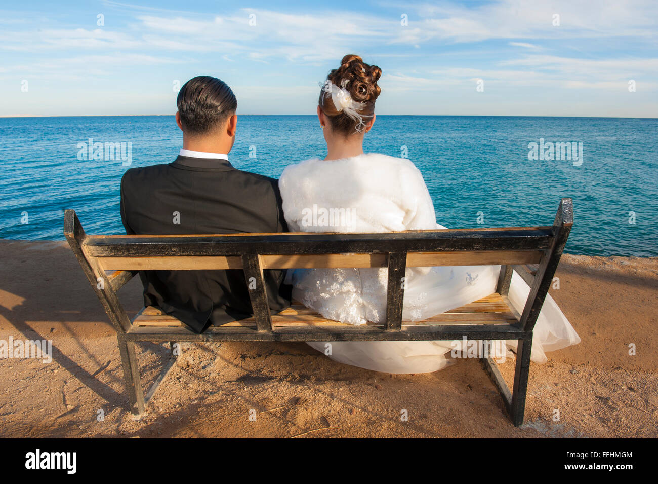 Sposa e lo sposo giovane seduto su una panca in legno affacciato sul mare tropicale Foto Stock