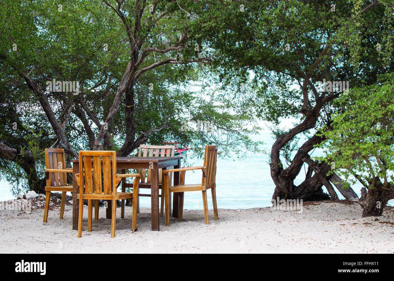 Posto romantico con un tavolo sulla spiaggia all'ombra degli alberi. Immagine di stock. Foto Stock