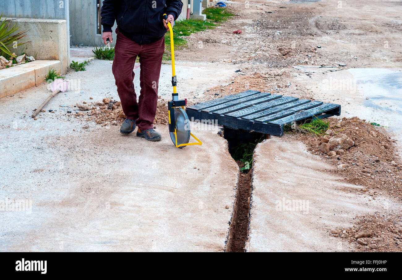 Geometra con ruota di misurazione (contachilometri) rileva la lunghezza di uno scavo di mini-trench Foto Stock