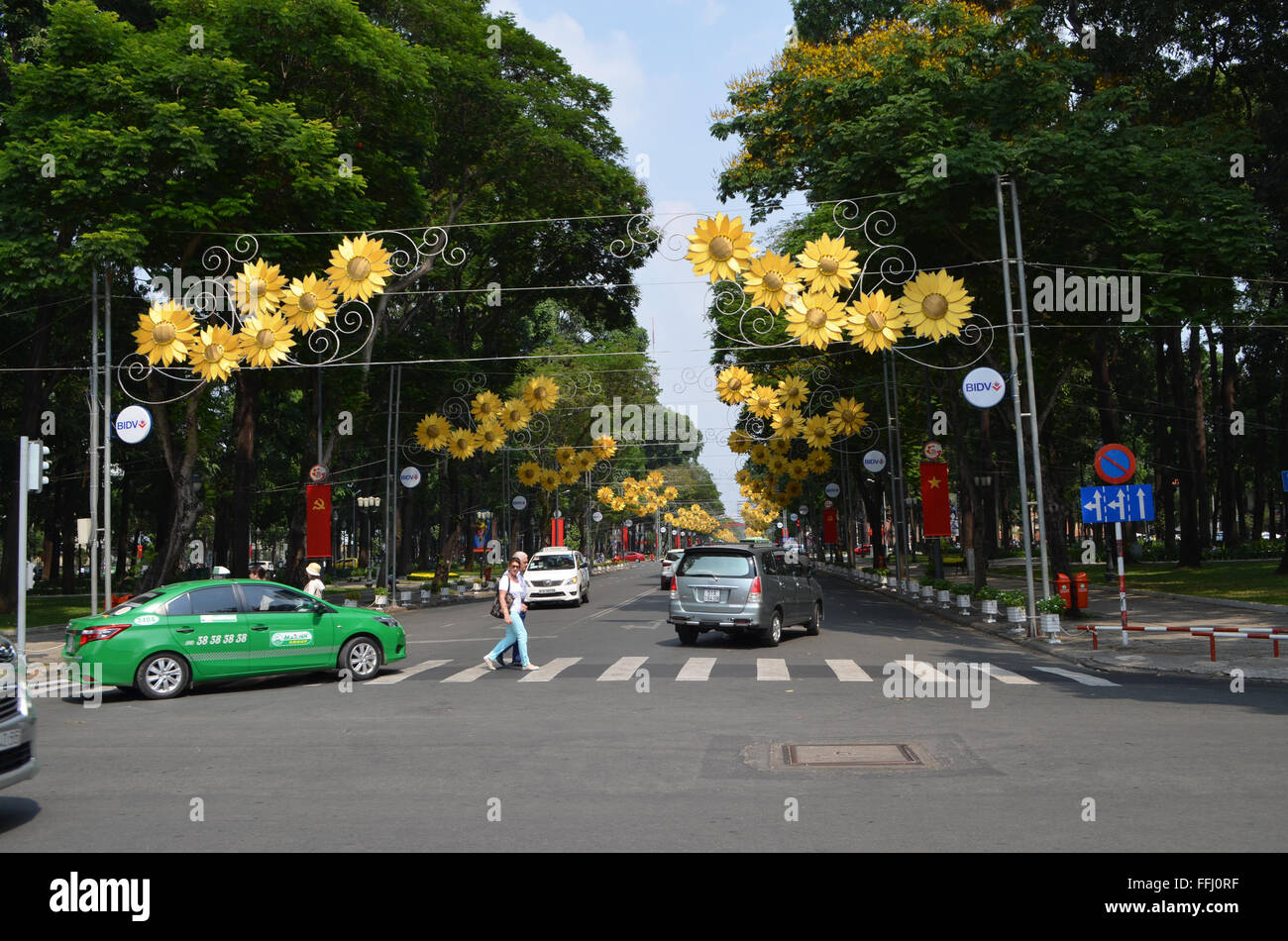 A Saigon, Vietnam le strade sono allegramente coveredwith bunting, bandiere, e questi fiori come persone travelon motociclette e auto piccole Foto Stock