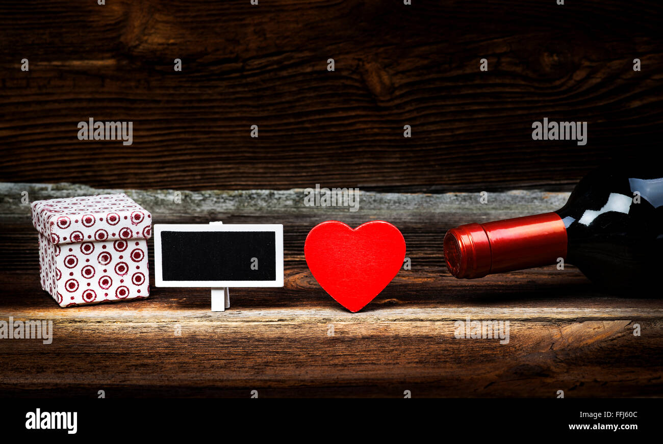 Rosso Cuore di legno, bottiglia di vino, confezione regalo e una piccola Lavagna sulla tavola di legno. Il concetto di amore nel Vintage. Il giorno di San Valentino. Foto Stock