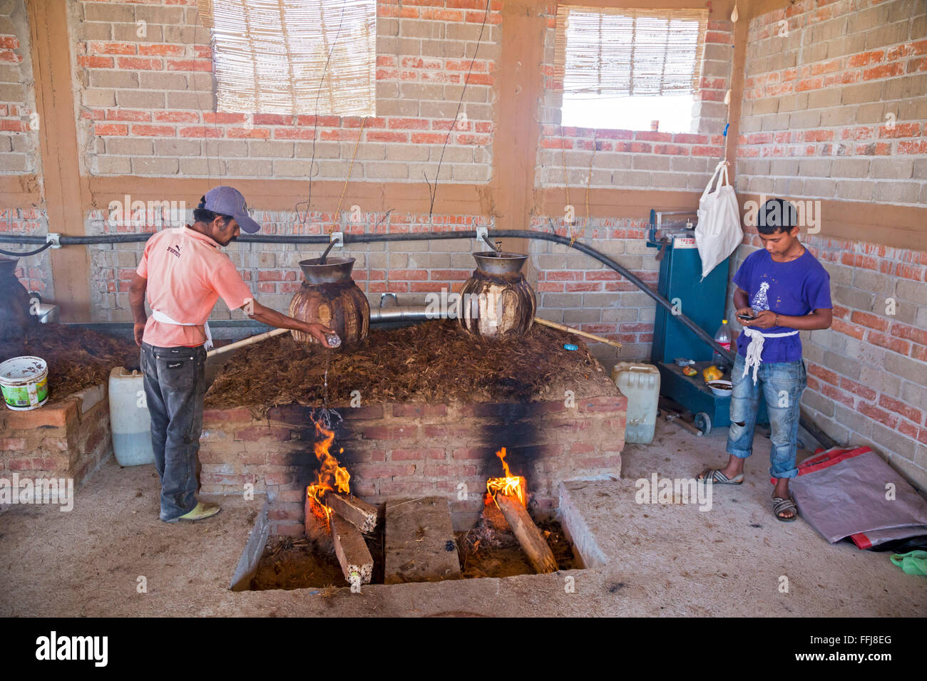 Santa Catarina Minas, Oaxaca, Messico - Mezcal distilleria. Un lavoratore dribbling acqua per inumidire il riscaldamento di fuoco una pentola di creta ancora. Foto Stock