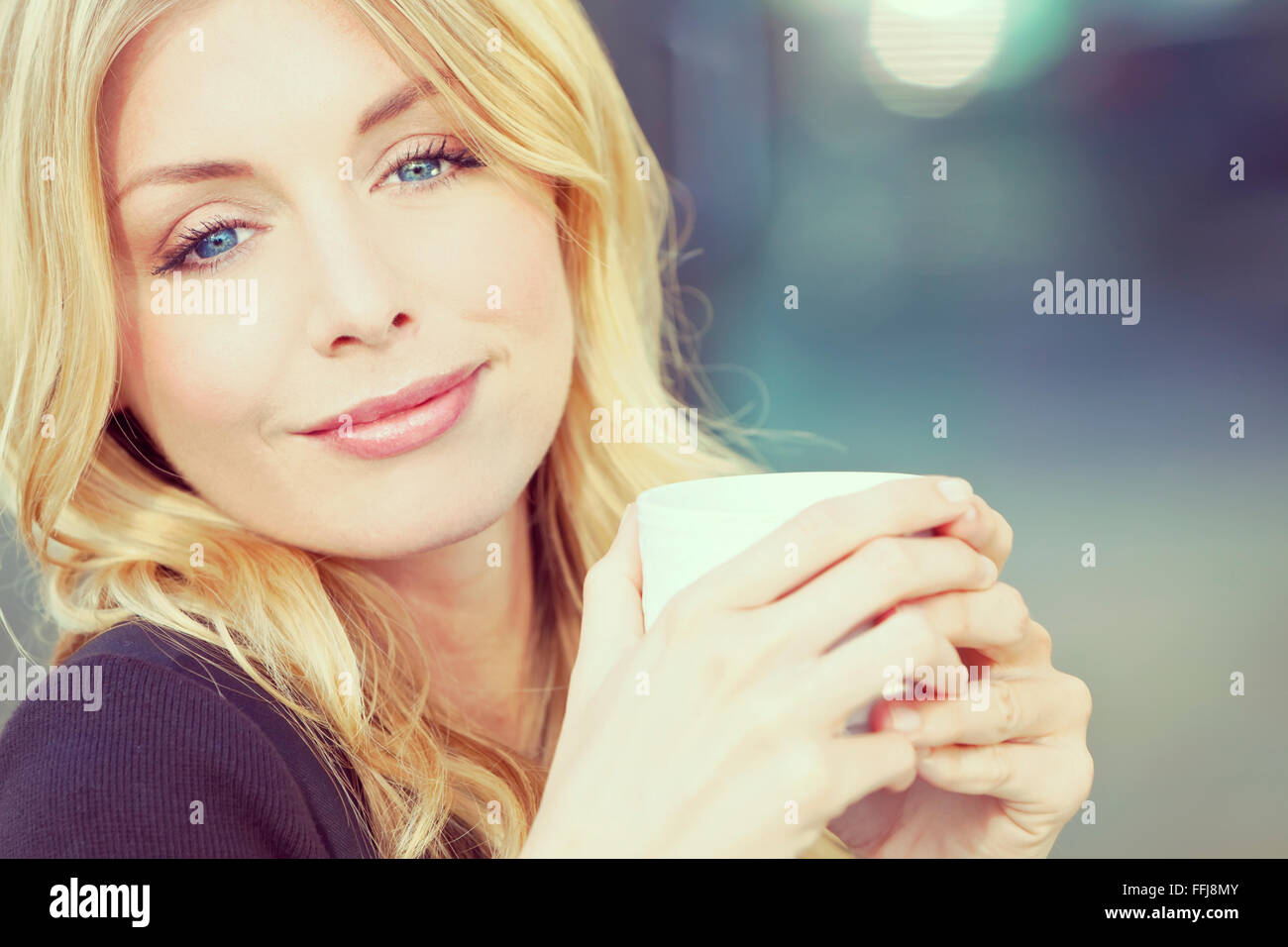 Un filtro Instagram ritratto di stile di una bella sorridente giovane donna  con i capelli biondi e gli occhi blu di bere il caffè o il tè da Foto stock  - Alamy
