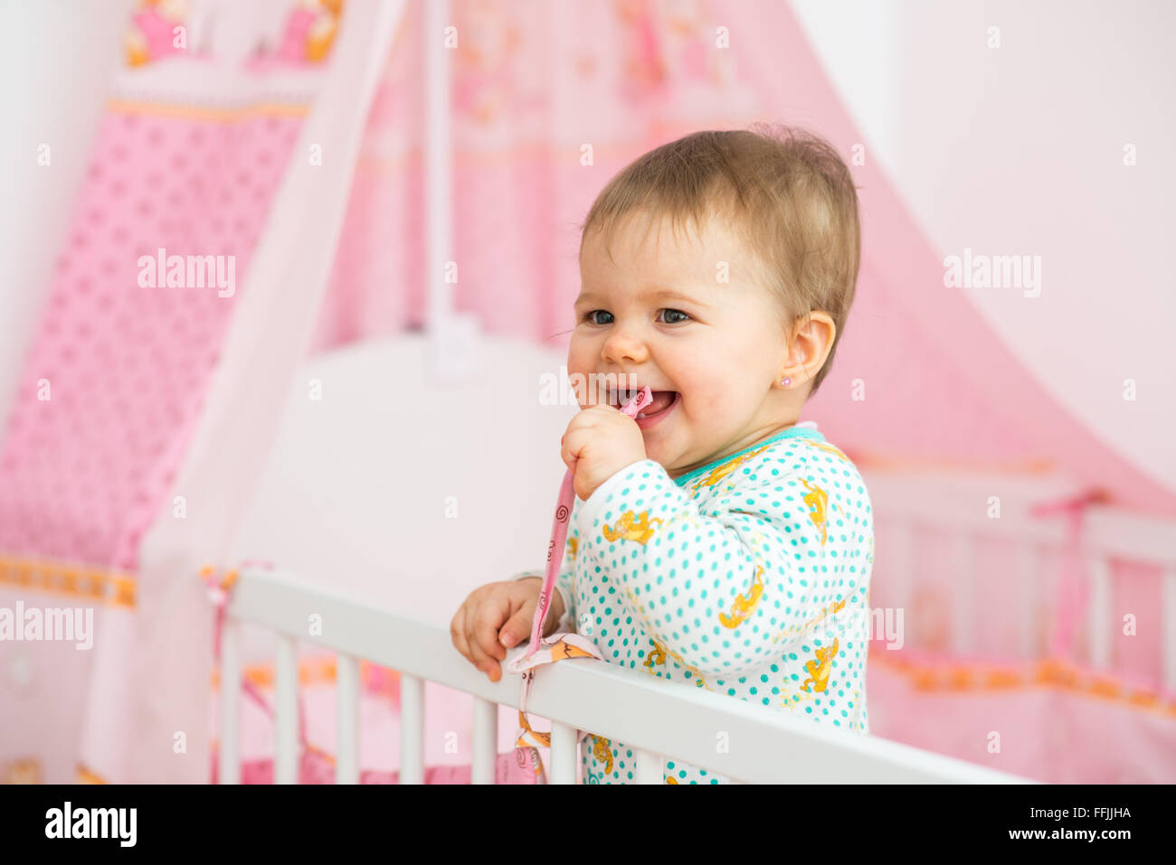 Baby girl è semplicemente in piedi nel letto nella stanza del bambino Foto Stock