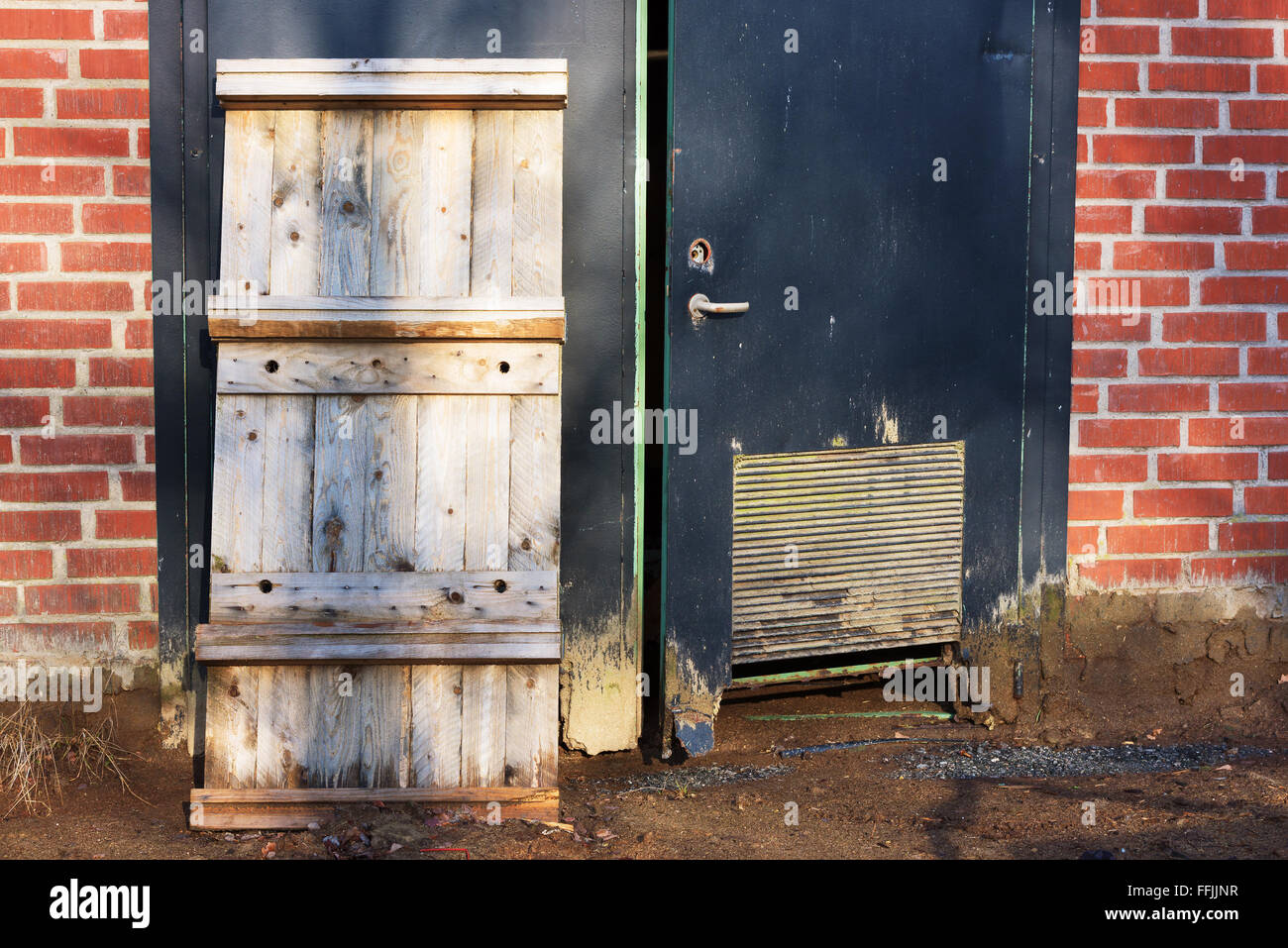 Un pallet di legno appoggiarsi contro un nero sportello in acciaio di un abbandonato edificio industriale. Foto Stock