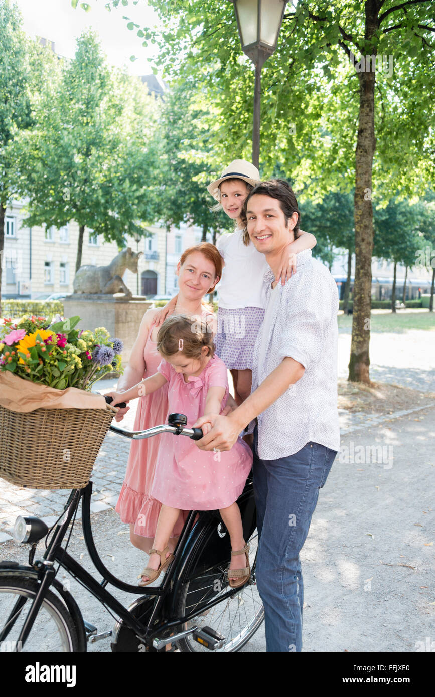Famiglia con due bambini spingendo in bicicletta in città Foto Stock