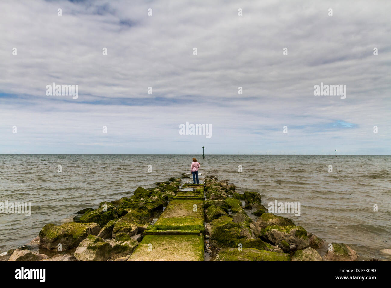 Signora matura in piedi alla fine di un interruttore d'onda jetty sul litorale di Colwyn Bay Foto Stock
