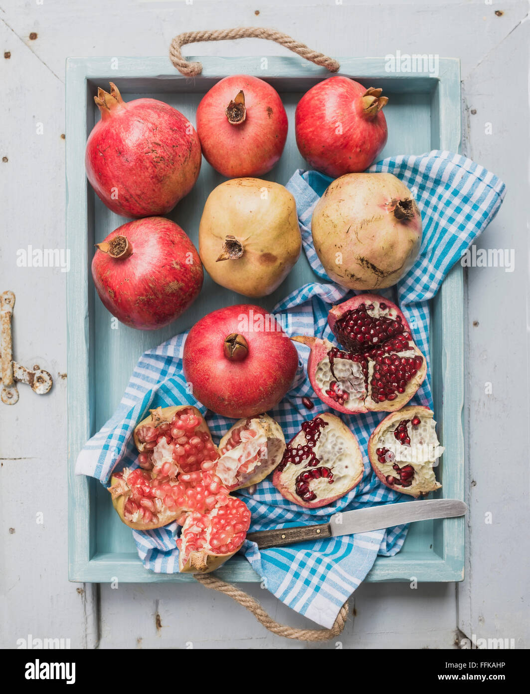 Il bianco e il rosso melograno e il coltello sul panno da cucina nel vassoio blu sulla luce dipinta sullo sfondo di legno, vista dall'alto Foto Stock